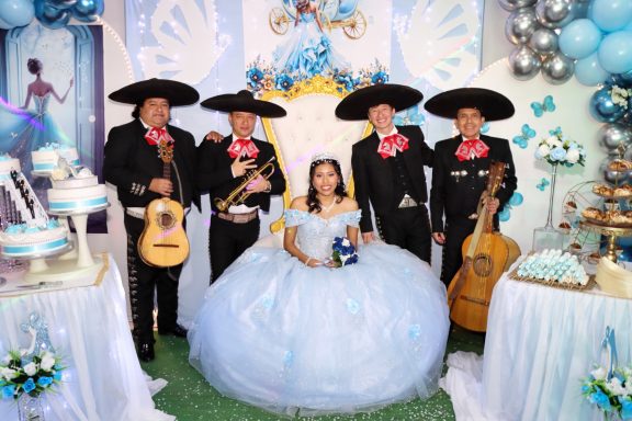 Celebración de quince años con la quinceañera y mariachi, decoraciones en azul.